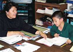 Photo of a teacher pointing out something in a book to a student.